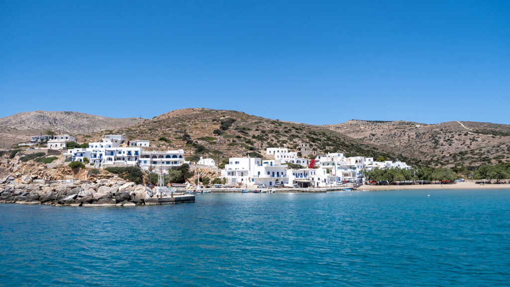 Sikinos island port, whitewashed buildings and blue sky background. Sandy beach and clear turquoise water. Summer holidays at a small Greek island, Cyclades, Greece